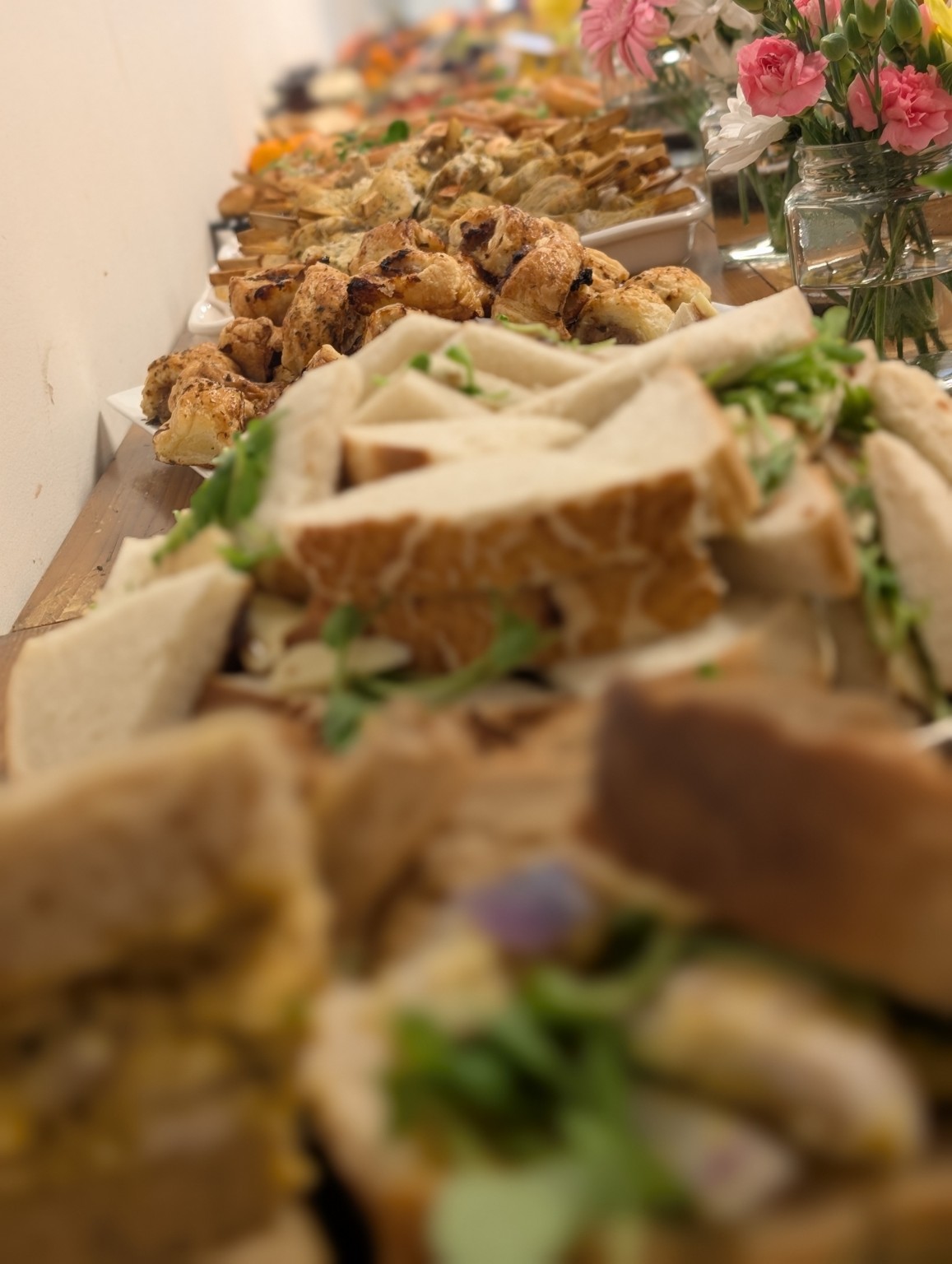 A long buffet table with sandwiches, savoury pastries and flowers