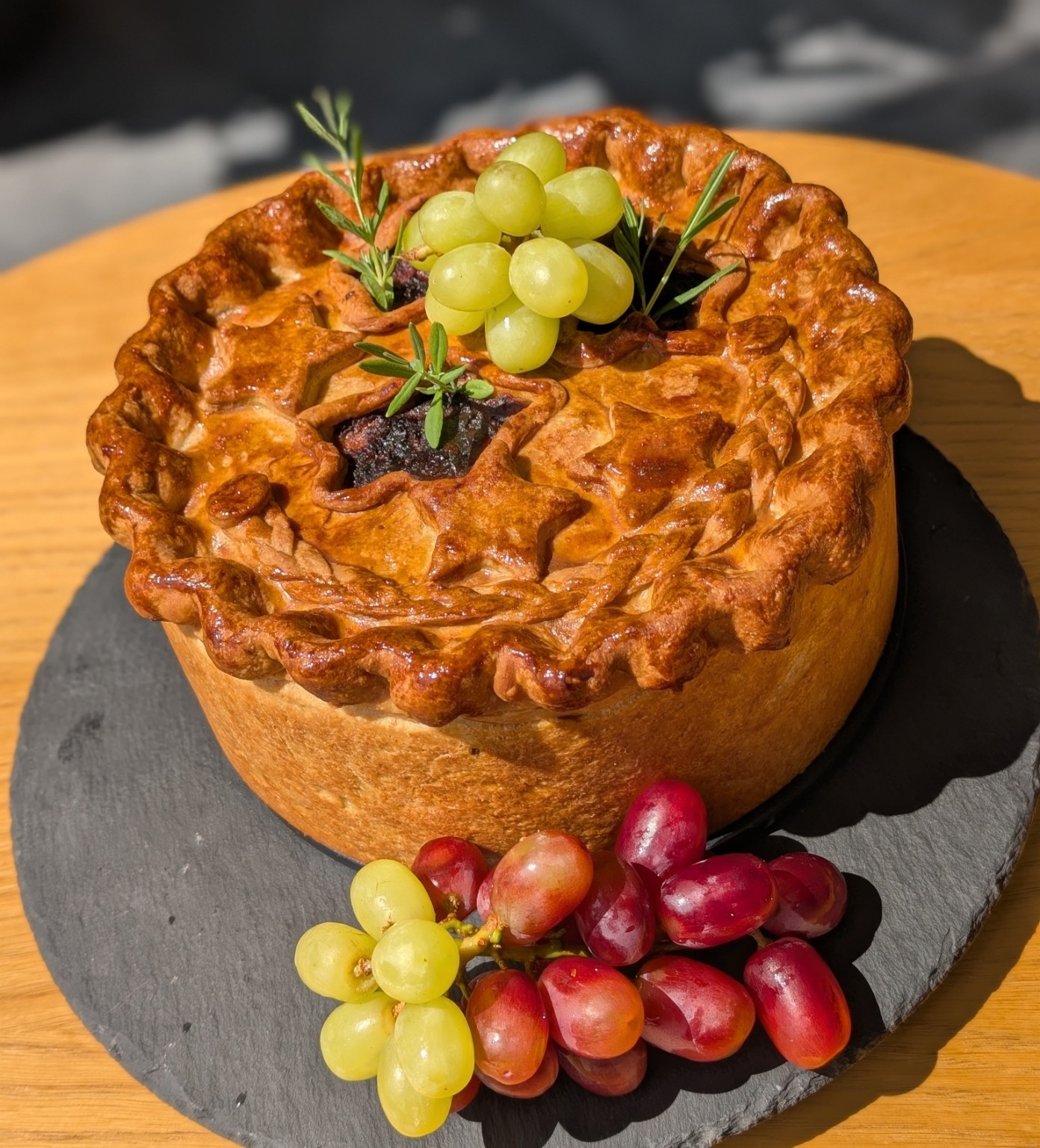 A golden decorated sharing pie presented with grapes and rosemary