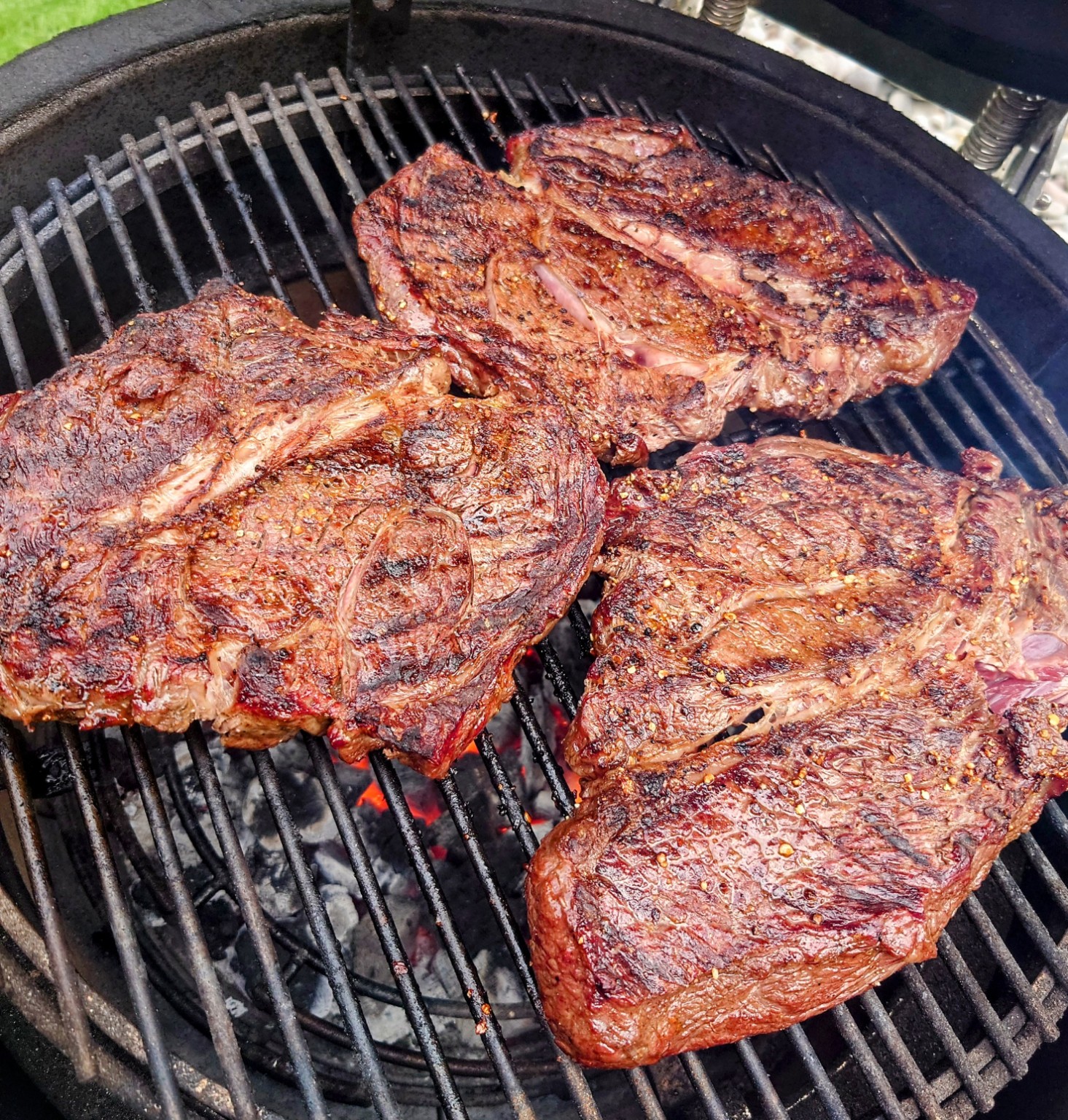 Large cuts of meat cooking over a charcoal grill