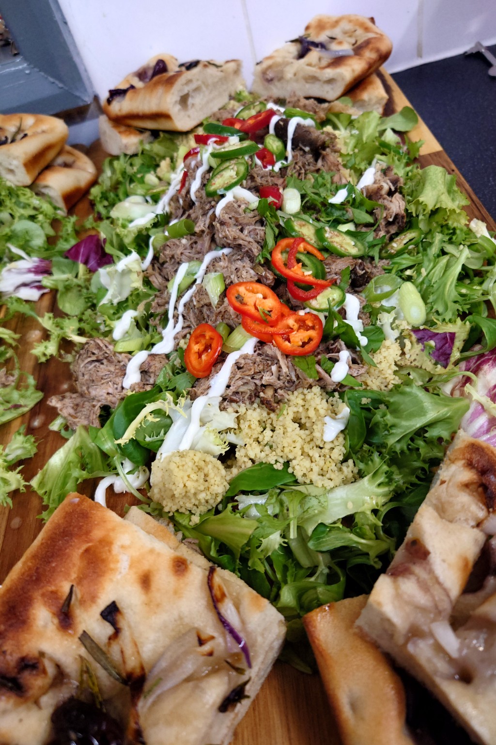 Pulled meat, leafy salad and grains surrounded by pieces of focaccia