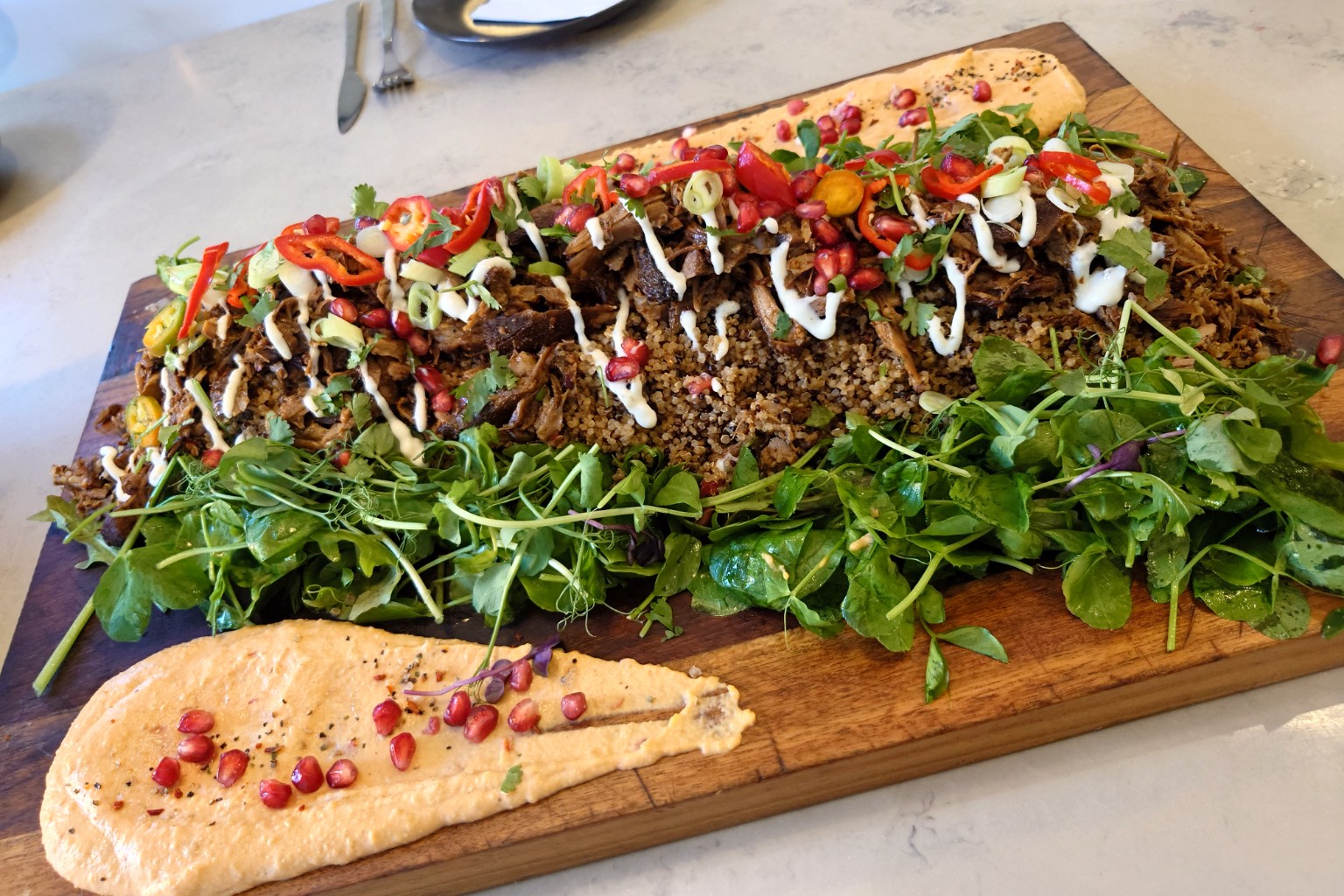 A generous sharing board with pulled meat, grains, greens and pomegranate